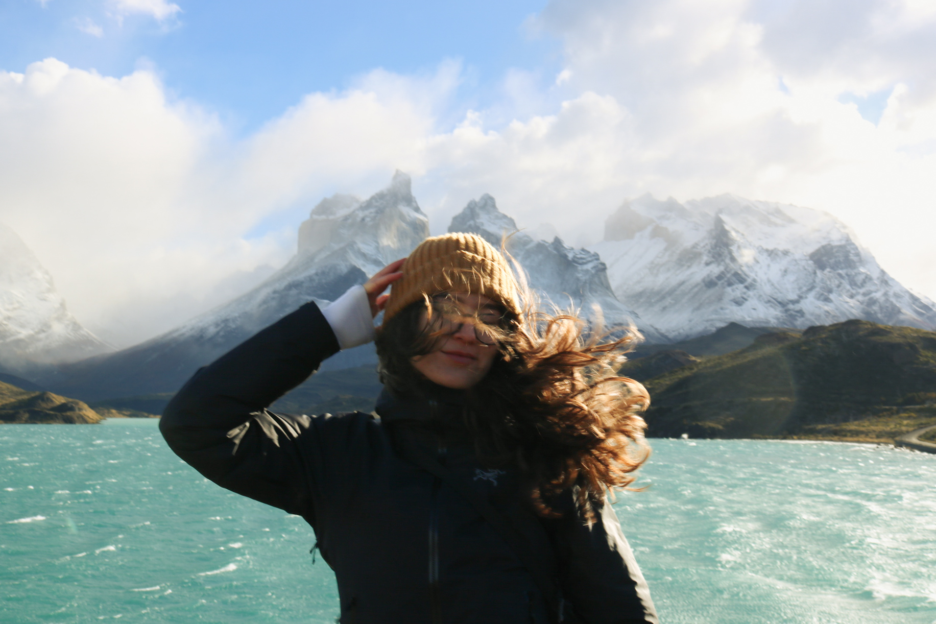 Windswept moment in front of the turquoise lake and snowy peaks of Patagonia